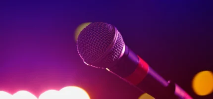 A closeup of a microphone with blurred stage lighting in the background.